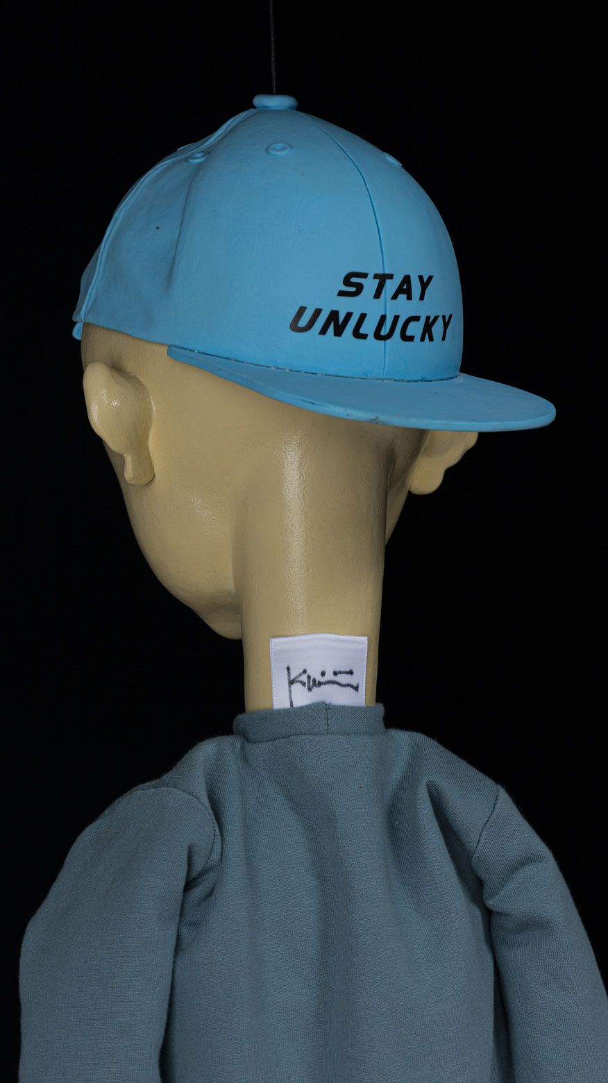 Bagside af skulpturen Stay Unlucky med blÃ¥ kasket og kunstnerens mÃ¦rkat.